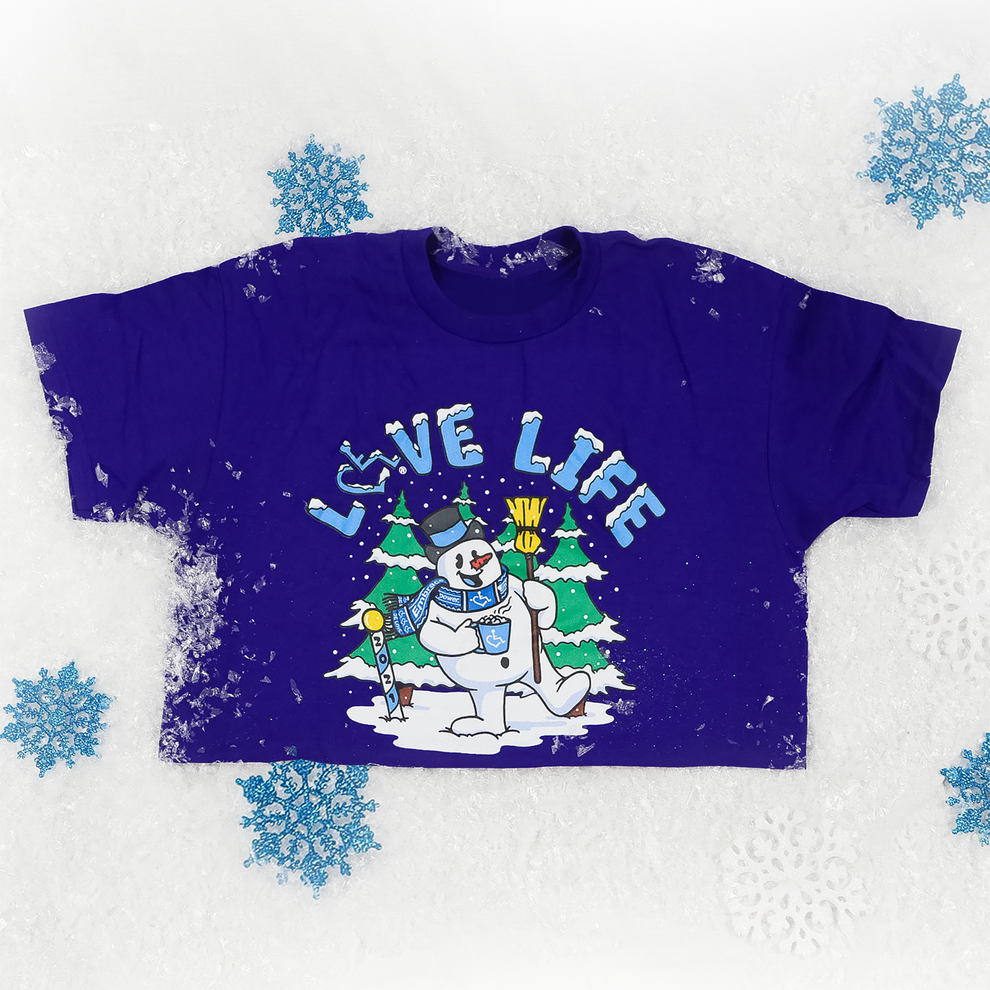 2021's limited edition short-sleeve t-shirt holiday design features a jolly snowman sporting a 3E Love knit scarf and holding a warm mug of hot cocoa
